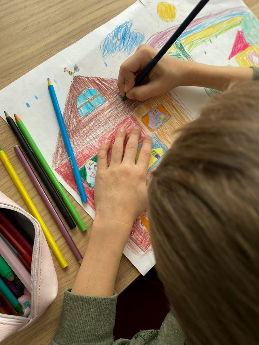 A child drawing a house with coloured pencils
