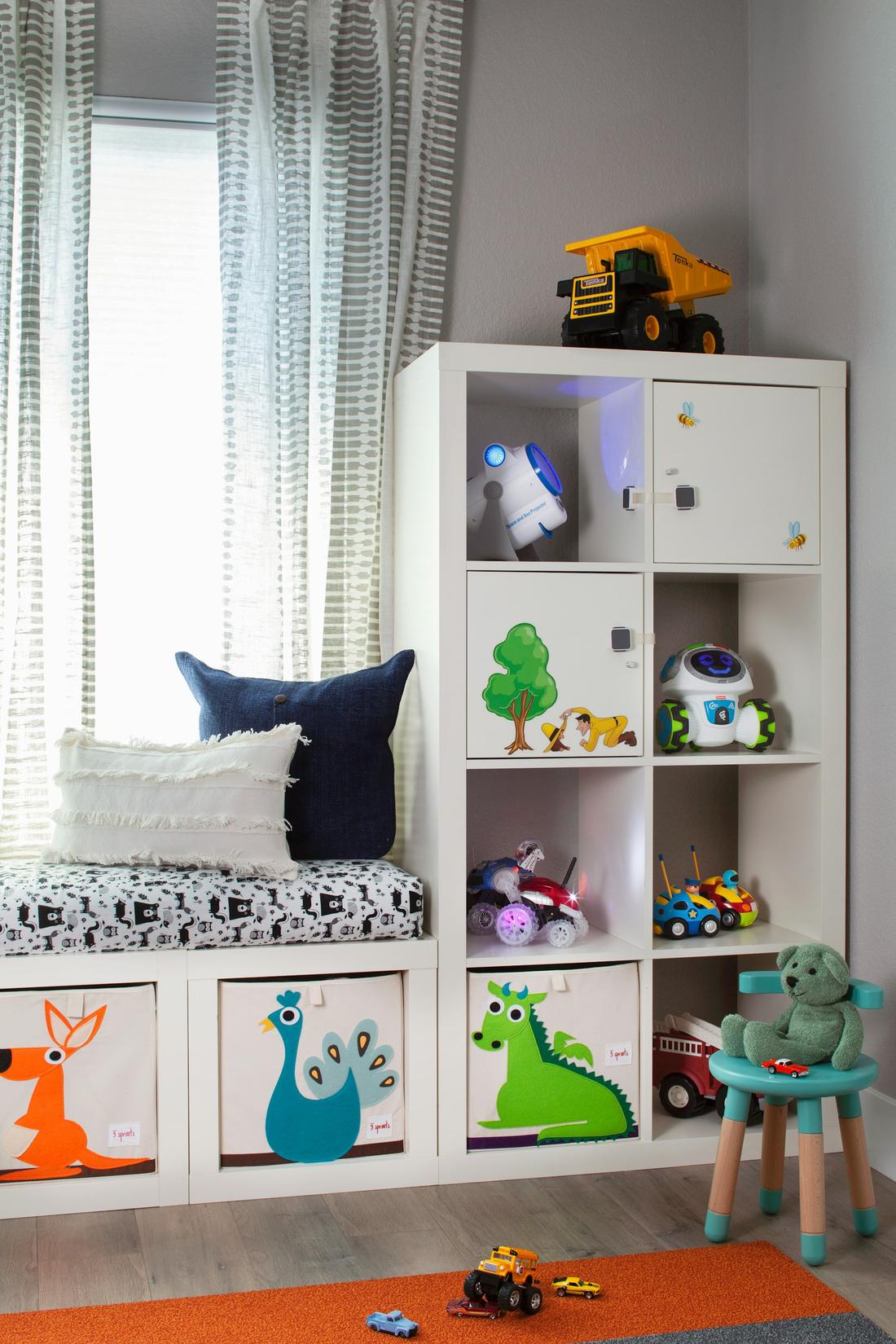 A children's room with a window seat and shelves of toys